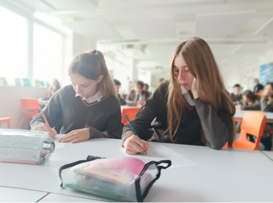 A group of girls sitting at a table writing on paper

Description automatically generated